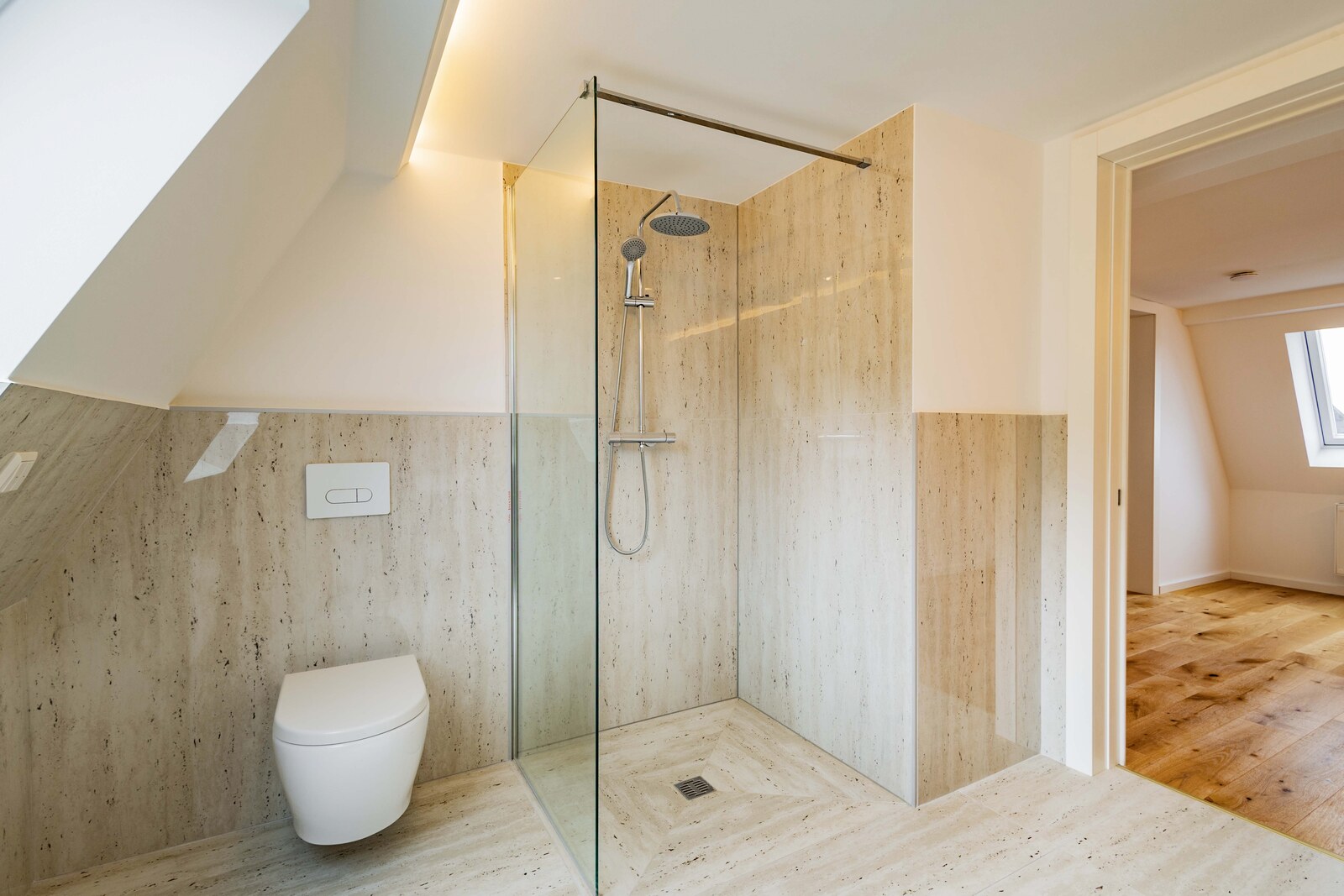 Bad mit ebenerdiger Regendusche hinter Glas, Travertin an Wand und Boden, Dachschräge — dahinter der Wohnraum mit Eichenparkett